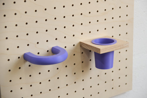 Anneau coloré violet fixé sur un pegboard en bouleau, à côté d'un pot suspendu violet