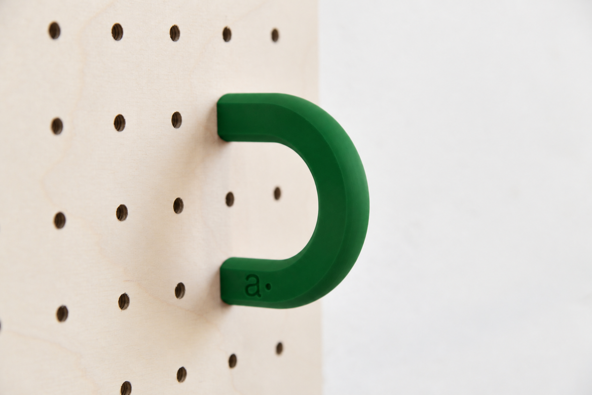 Anneau coloré vert foncé taille M sur un pegboard en bouleau