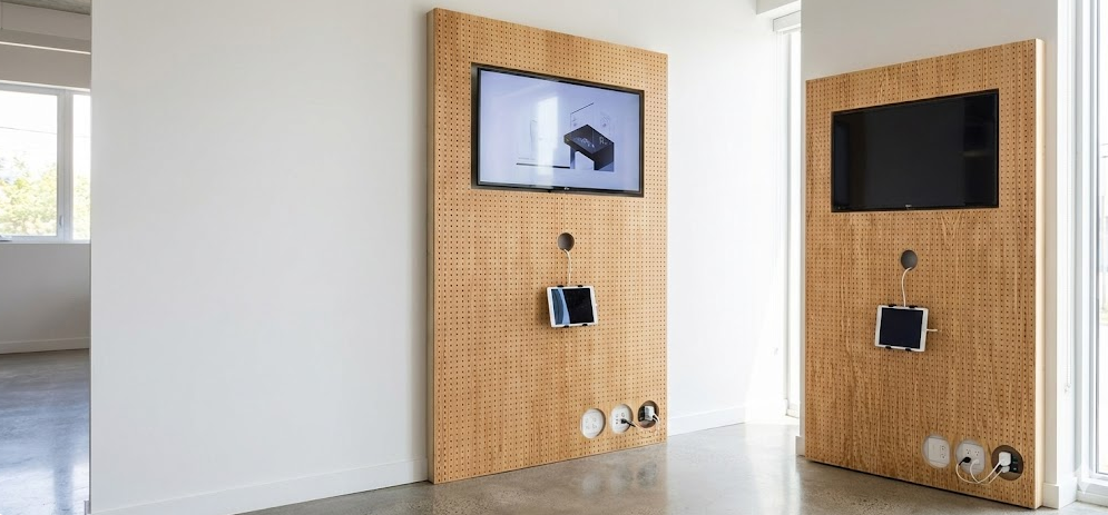 Two wooden pegboard wall organizers with mounted screens and attached devices in a bright modern room