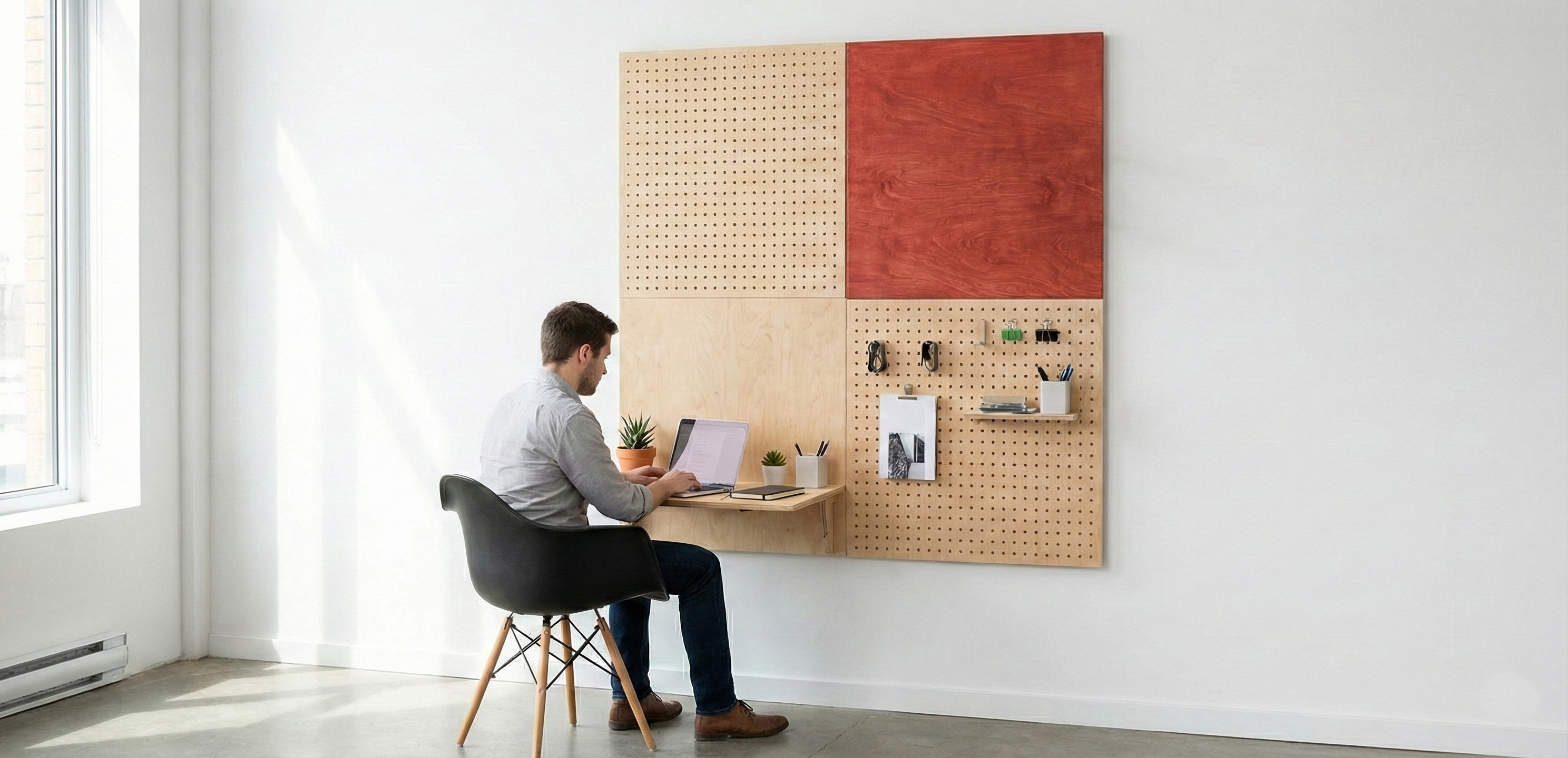 Man sitting at a wall-mounted modular pegboard shelf with pegboard accessories in a minimal workspace